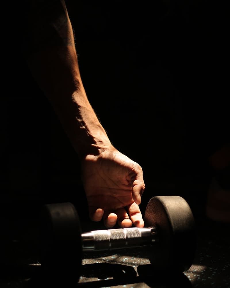 Close-up of a hand gripping a dumbbell on the floor of a dimly lit gym.